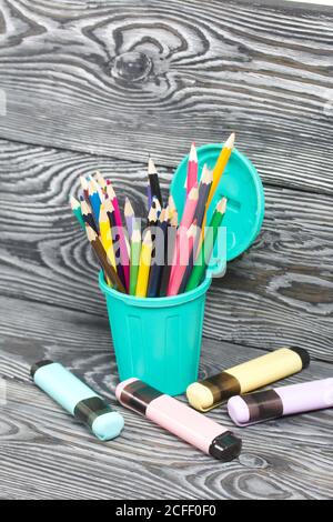 Colored pencils in a pencil holder. A pencil case in the form of a trash can. Nearby are colored markers. On brushed pine boards painted black and whi Stock Photo