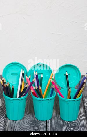 Colored pencils in pencil holders. A pencil case in the form of a trash can. On brushed pine boards painted black and white. Stock Photo