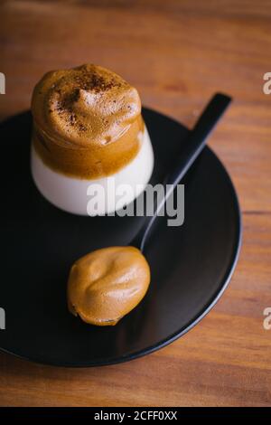 Top view of tasty Dalgona drink prepared from cold milk and whipped coffee on a glass placed on a black plate on a wooden table Stock Photo