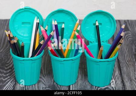 Colored pencils in pencil holders. A pencil case in the form of a trash can. On brushed pine boards painted black and white. Stock Photo
