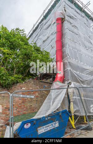 Red rubbish chute going into a skip on a building construction site in the UK. Stock Photo