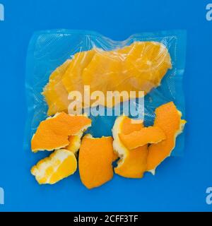 Top view of ripe peeled orange in vacuum plastic bag and orange peel on blue background Stock Photo
