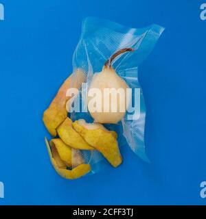 Top view of ripe yellow peeled pear in vacuum plastic bag and pear peel on blue background Stock Photo