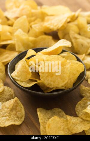 Bowl with pile of crispy potato chips placed on wooden table in kitchen Stock Photo