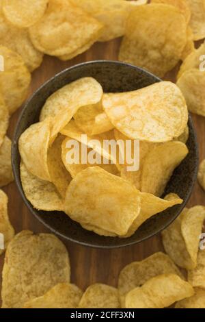 Bowl with pile of crispy potato chips placed on wooden table in kitchen Stock Photo