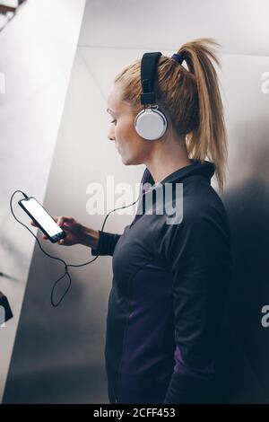 Young blonde caucasian Woman with sportswear listening to music with headphones connected to her smartphone Stock Photo
