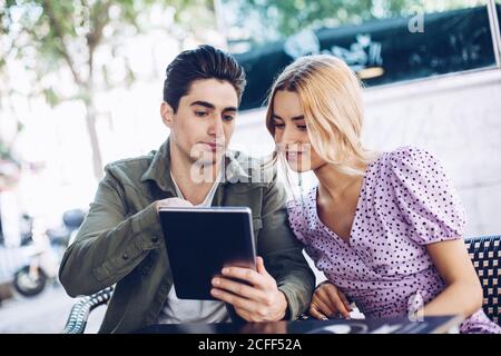 Cheerful young attractive couple using tablet outdoors in town in warm day Stock Photo