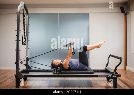 Side view of adult female in sportswear lying on pilates machine and doing exercises with resistance bands Stock Photo