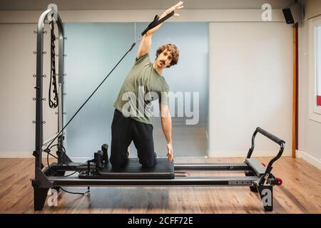 Sportsman in activewear using pilates machine and stretching arms with resistance bands Stock Photo