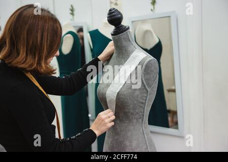 anonymous Woman with tape measure attaching paper cutout to mannequin with pin while making clothes in professional workshop Stock Photo