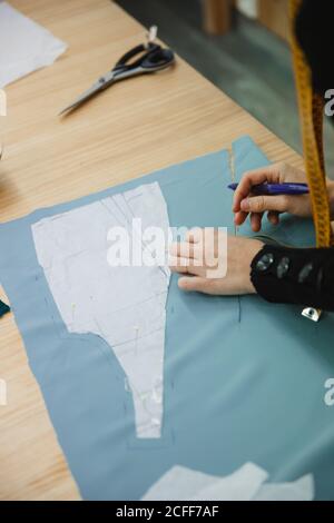 Adult lady using tape to measure garment part on table during work in professional dressmaking workshop Stock Photo