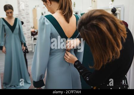 unrecognizable dressmaker fitting custom gown on back of female client while working in professional workshop Stock Photo