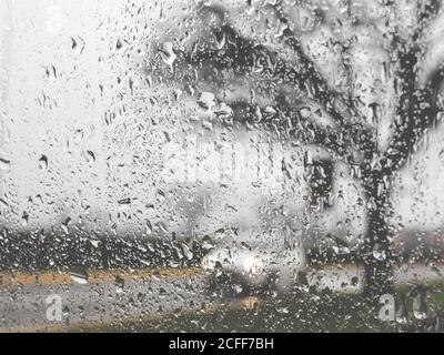 Rainy bad weather on the street. Raining and wet weather driving conditions on the road, traffic blurred, raindrops on car windscreen. Stock Photo