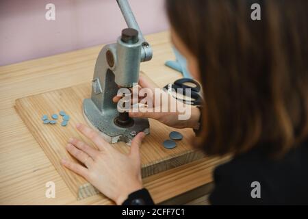 From above anonymous Woman using shabby button maker on workbench in tailor studio Stock Photo