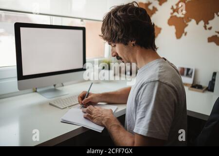 Side view of man entrepreneur taking notes in notebook while working remotely at home Stock Photo