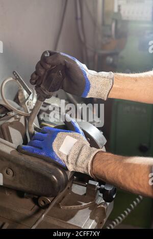 Crop faceless male in gloves creating details while working on industrial machine at workshop Stock Photo