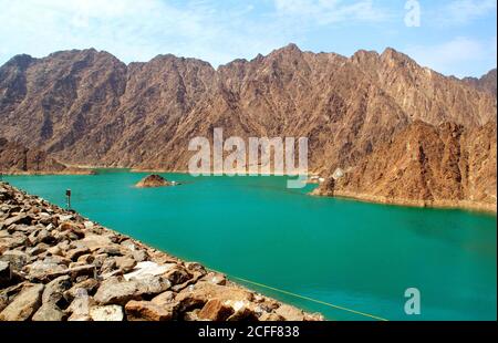 Beautiful deep green Hatta lake with rocky Hajar Mountains on background. Overview of Hatta dam in UAE, Oman. Picturesque nature in the Middle East. Stock Photo