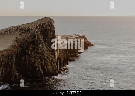 Coastal cliffs and Neist Point lighthouse near sea against clear blue sky on sunny day Stock Photo