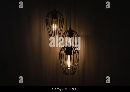 Hanging metal wired lanterns with glowing light bulbs illuminating dark room in Navarre, Spain Stock Photo