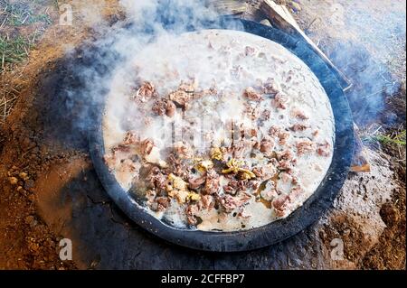 A big traditional pot on an open fire place containing cooking meat and intestines stew, fire wood and smoke around the pot, Sagada, Philippines Stock Photo