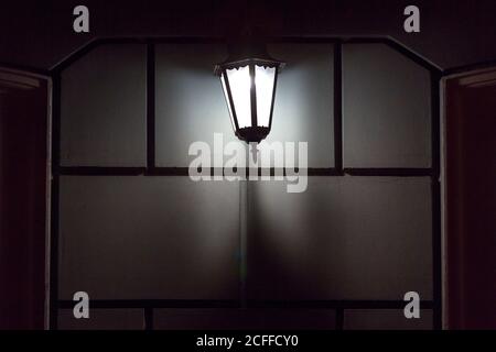 black iron retro lantern with glass hanging on the wall of the facade of the building illuminating the architecture of the city at night, closeup glow Stock Photo