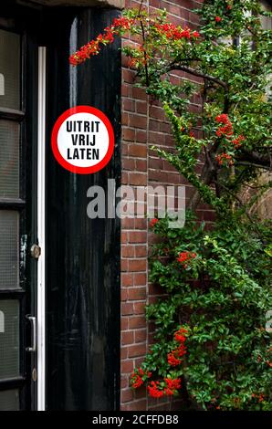 Black door frame with a 'Keep exit clear' sign in Dutch and a bush with red berries near it. Focus on the sign, shallow depth of field. Stock Photo