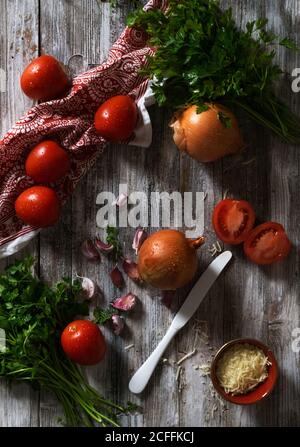 From above Fresh ripe tomatoes and onions with garlic and parsley placed on shabby wooden tabletop near napkin Stock Photo