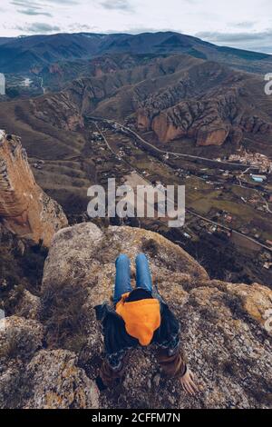 Top view of anonymous Woman sitting on rock at edge of cliff with picturesque view Stock Photo