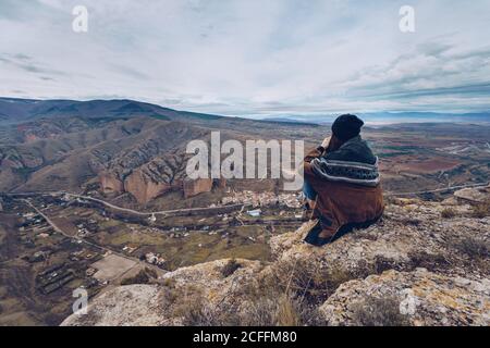 Back view of anonymous Woman sitting on rock at edge of cliff with picturesque view Stock Photo
