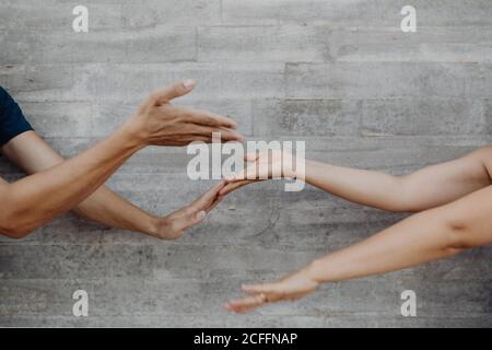 Tanned strong hands of crop man and Woman gesturing and showing up and down on background of grey wall Stock Photo