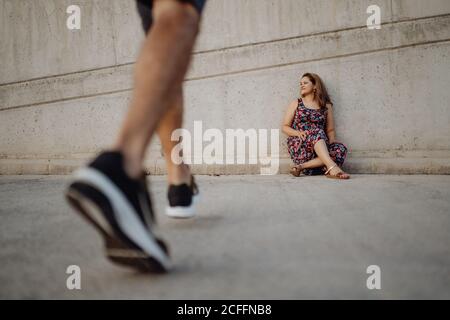 woman sitting on grey wall while crop man is walking to her