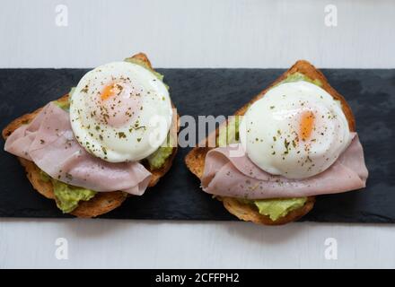 From above of appetizing toasts with guacamole garnished with tasty fried eggs and ham placed on table for breakfast Stock Photo