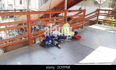 A blind beggar is begging at the foot over-bridge. Mother is lying beside her. Poor son, poor mother photo. Stock Photo