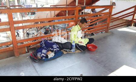 A blind beggar is begging at the foot over-bridge. Mother is lying beside her. Poor son, poor mother photo. Stock Photo