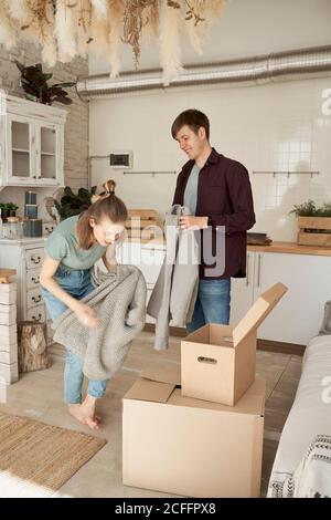 Happy young couple taking out soft gray sweaters and things in carton boxes in white light kitchen Stock Photo