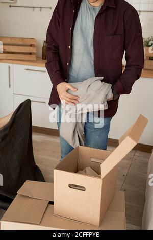 unrecognizable man taking out soft gray sweaters from carton boxes in white light kitchen Stock Photo