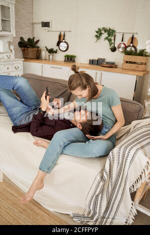 Calm thoughtful young man and Woman lying on cozy soft couch and surfing mobile phones at home Stock Photo