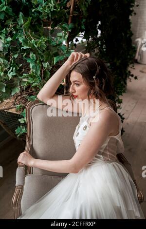 Gorgeous Woman with red lips in white dress sitting on armchair Stock Photo
