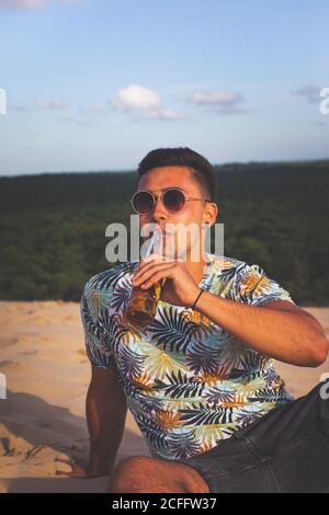 Young caucasian man drinkin beer at the top of a sand dune. Stock Photo