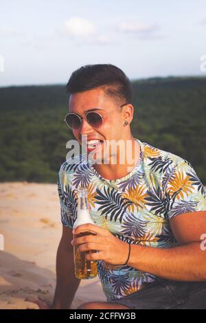 Young caucasian man drinkin beer at the top of a sand dune. Stock Photo