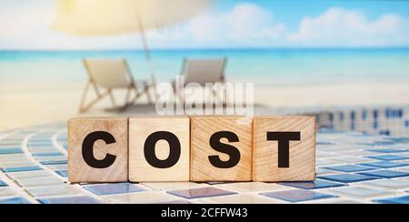 Wooden cubes form the word 'cost' near ocean landscape Stock Photo