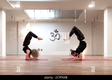 Side view of young man and Woman in sportswear bending back while doing yoga exercise during training in spacious studio Stock Photo