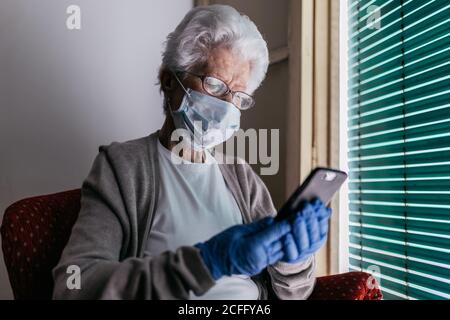 Senior Woman chatting on smartphone during self isolation at home Stock Photo
