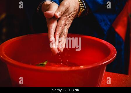 faceless religious person placing hands in red bowl with water washing hands for ritual Stock Photo