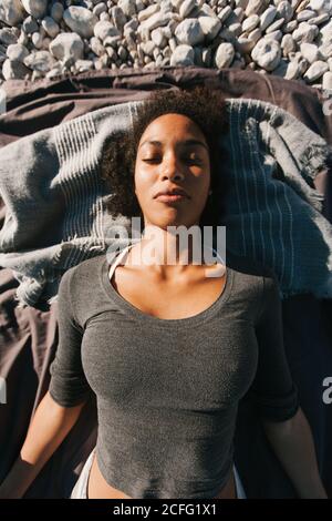 From above portrait of African American attractive young Woman meditating lying on the ground at the beach Stock Photo