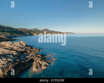 The rocky coastline and turquoise Mediterranean sea in the Balagne region of Corsica with the port of Ile Rousse in the distance Stock Photo