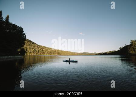 Silhouette of anonymous male traveler sitting on kayak and rowing during trip on calm river on cloudless day in La Mauricie National Park in Quebec, Canada Stock Photo