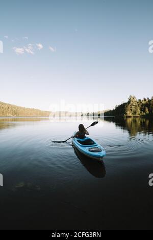 Silhouette of anonymous female traveler sitting on kayak and rowing during trip on calm river on cloudless day in La Mauricie National Park in Quebec, Canada Stock Photo