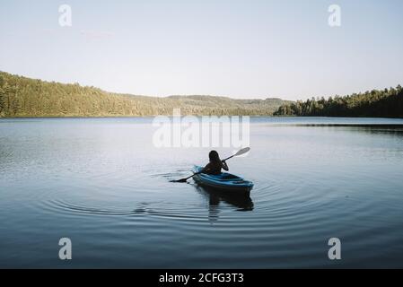 Silhouette of anonymous female traveler sitting on kayak and rowing during trip on calm river on cloudless day in La Mauricie National Park in Quebec, Canada Stock Photo