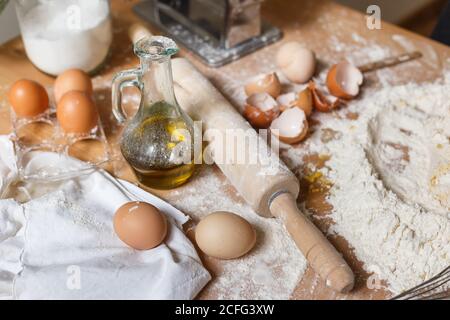 From above of messy table in process of making dough with flour wooden rolling pin and ingredients for pasta at home Stock Photo
